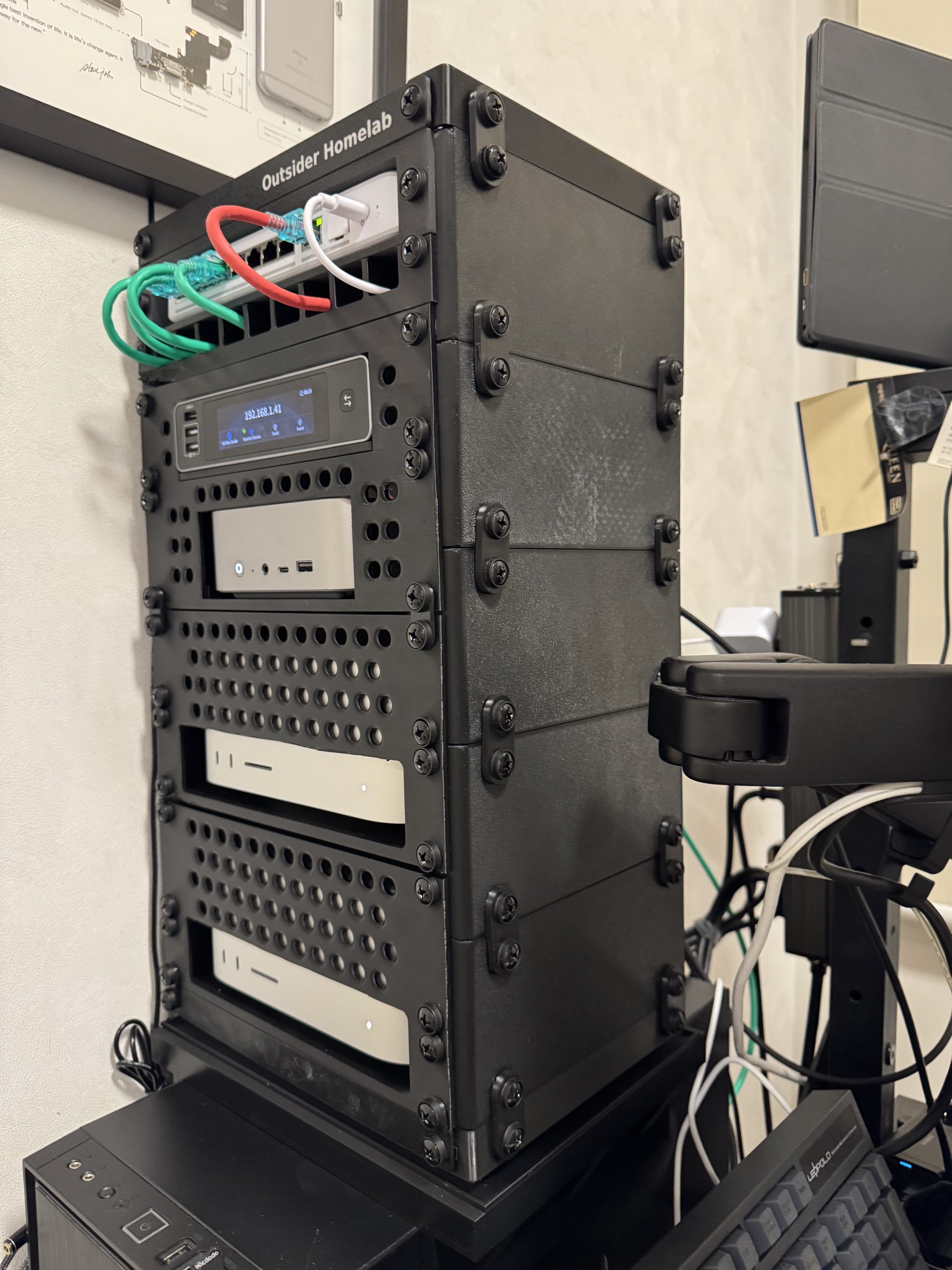 Outsider Homelab 라벨이 붙은 검은색 미니 랙에 네트워크 스위치, IP 주소를 띄운 디스플레이 패널, 미니 PC와 맥 미니 두 대가 층층이 장착되어 있다.